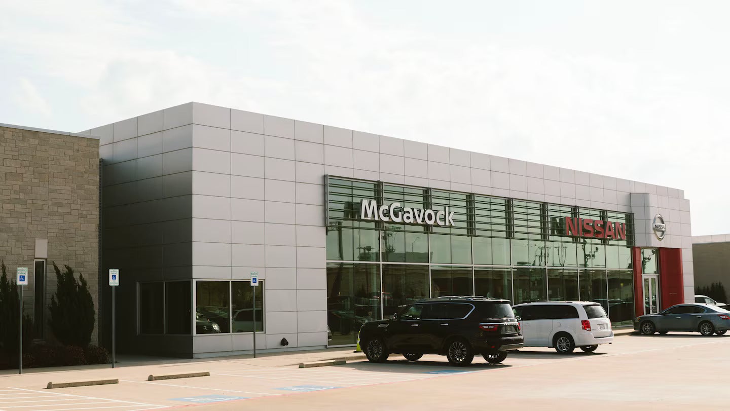 A sleek McGavock Auto Group Auto Group dealership building with large glass windows, branded signage McGavock Auto Group and a few cars parked in front.